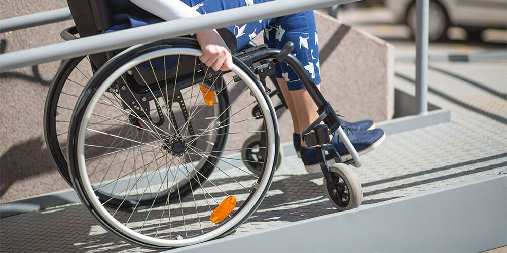 person in wheelchair going up an aluminum wheelchair ramp