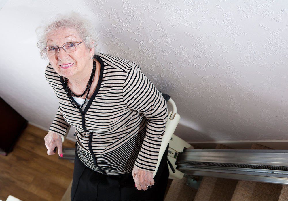 Image elderly woman riding up stair lift in home