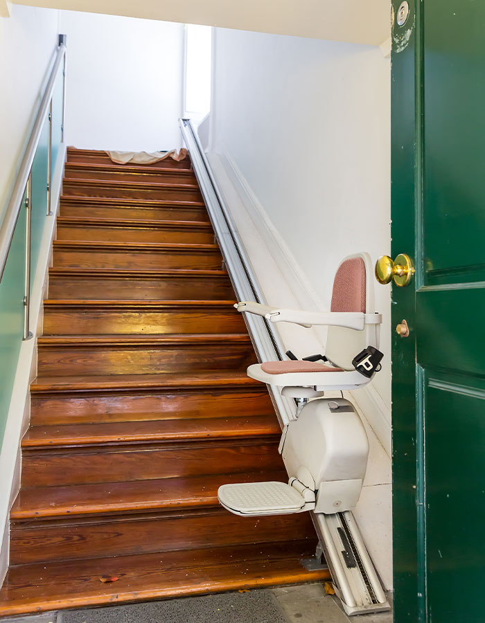 Image of a straight stair lift at the bottom of a staircase in a hallway