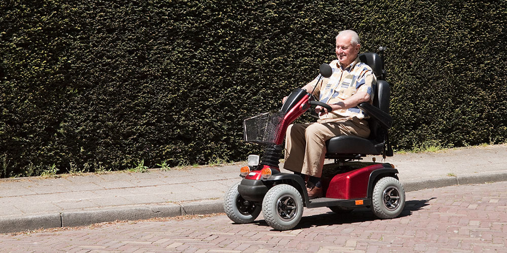 Image of old man driving four wheeled mobility scooter down the street